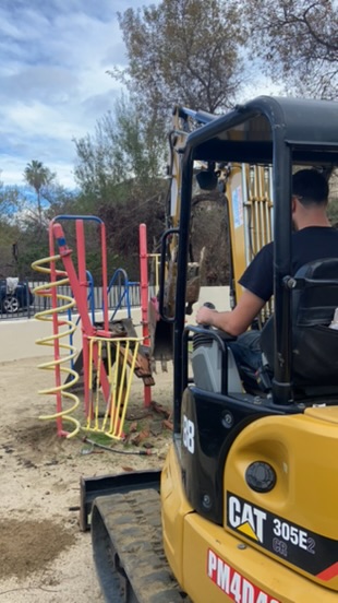 worker in safety gear demolishing red structural steel beams with yellow excavator